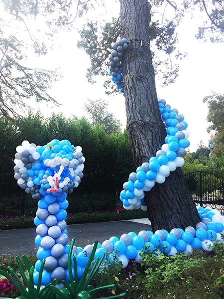 A giant 30 foot long serpent of blue balloons partially coiled in a large tree is one of the decorations for a children's birthday party..