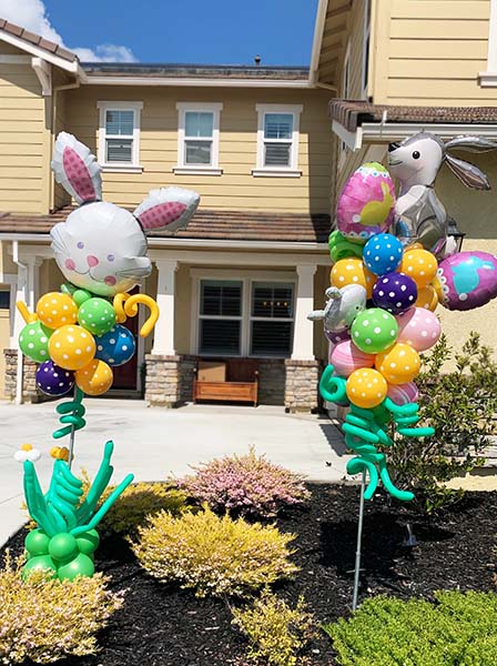 Two easter theme decorations made with mylar and latex balloons on poles placed in the yard of a residence