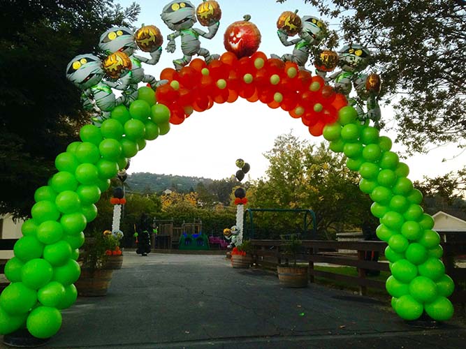 This lime green and orange swirled-style balloon arch is topped by floating Halloween critters serving as the entrance decoration for a Halloween event