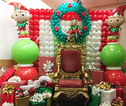 A gold adorned chair for visits from Santa framed by colorful holiday color balloons.